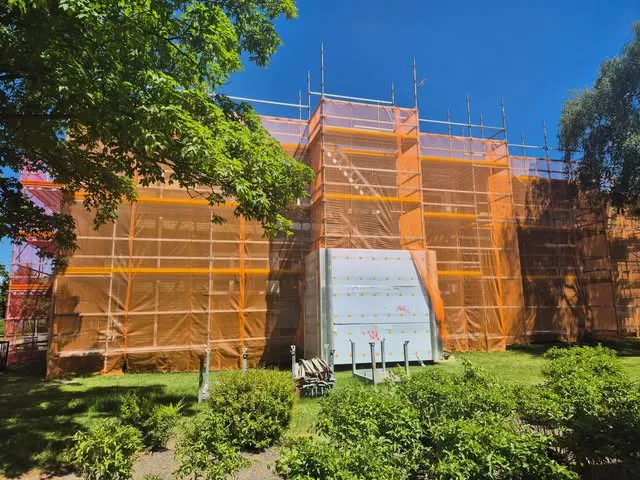 Flerbostadshus inklätt i orange väderskydd och fasadställning en solig sommardag