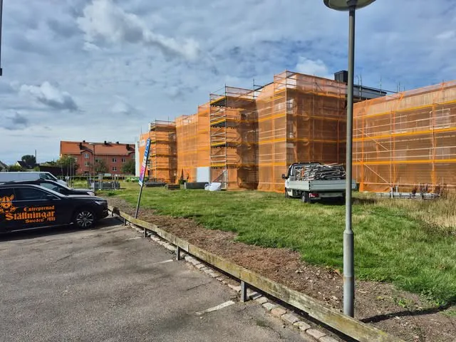 Rad av bostadshus i ställning med orange väderskydd, firmabil med Entreprenad Ställningars logotyp i förgrunden