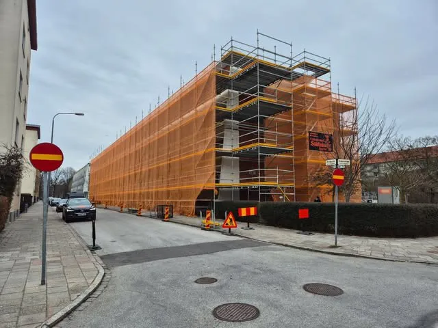 Hus helt inklätt i orange skyddsnät med ställning i flera våningar, sett från gatan