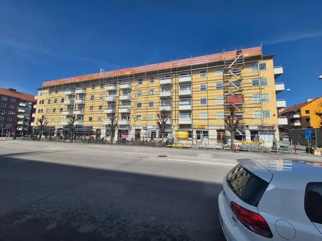 Gult flerbostadshus med fasadställning längs hela gatufasaden